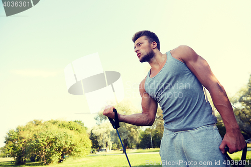 Image of young man exercising with expander in summer park