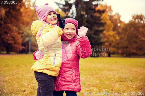 Image of happy little girls waving hands in autumn park