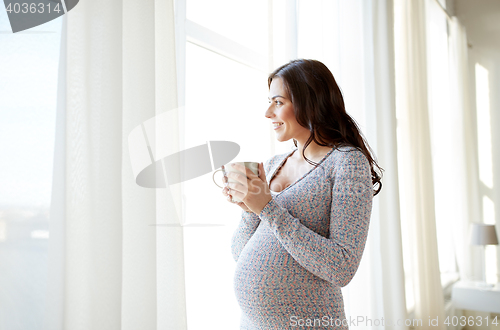 Image of happy pregnant woman with cup drinking tea at home