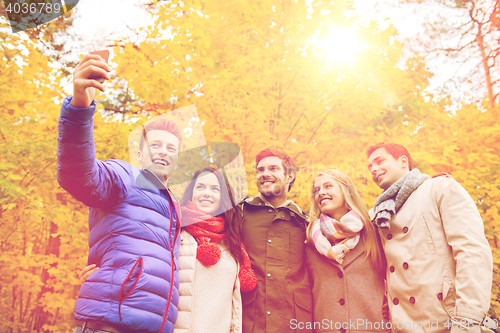 Image of smiling friends with smartphone in city park