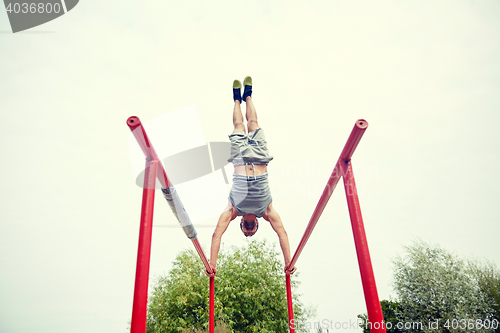 Image of young man exercising on parallel bars outdoors