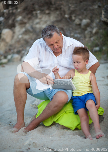 Image of Grandfather and grandchild using pad on the beach