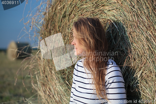 Image of Young woman by the hay roll in the field
