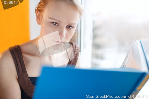 Image of Young woman reading a book with blue cover