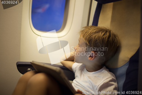 Image of Boy in plane looking out illuminator with pad on lap