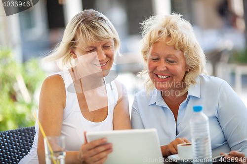 Image of Two women friends using tablet PC in outdoor cafe