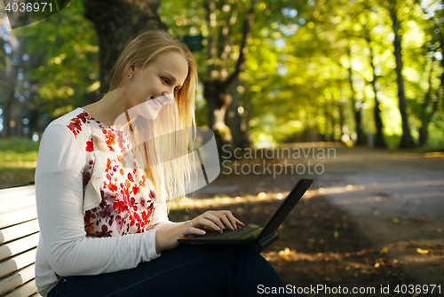 Image of Young woman using her laptop in the park