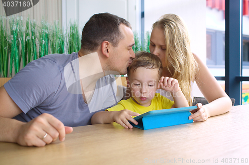 Image of Parents kissing son playing on pad