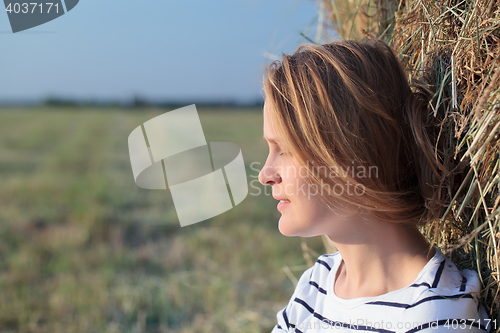 Image of Relaxed woman near hay roll in the field