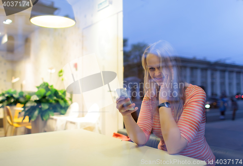 Image of Smiling woman in cafe reading or typing sms