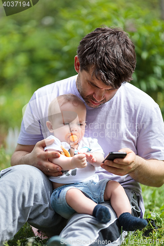 Image of Father using a mobile with baby on his lap