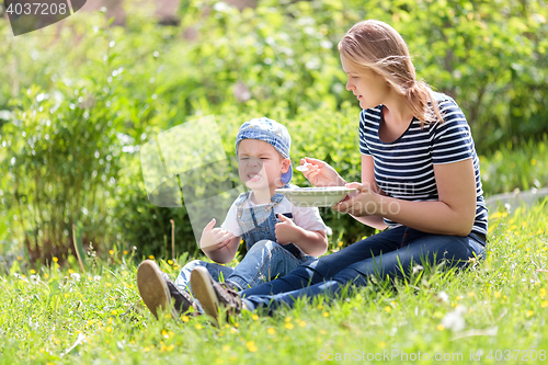 Image of Cute little boy being fed outdoors on the grass