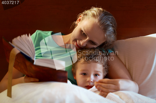 Image of Young mother reading to her child in bed