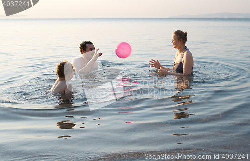 Image of Young family playing with ball at sunset