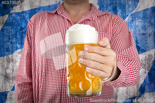 Image of Man in traditional Bavarian shirt holds mug of beer