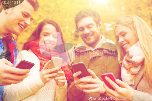 Image of smiling friends with smartphones in autumn park