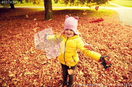 Image of happy girl playing with autumn leaves in park