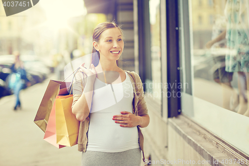 Image of happy pregnant woman with shopping bags at city