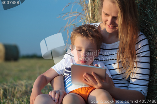 Image of Mother and son with pad sitting by hay roll in the field