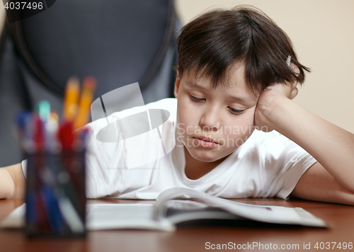 Image of School boy studies hard over his book at home.