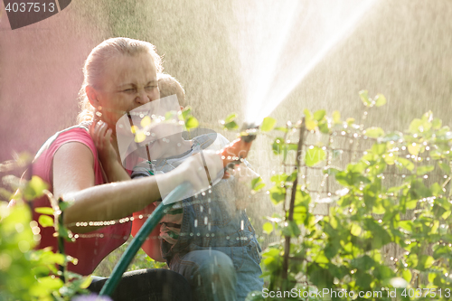 Image of Laughing mother and son playing with a sprinkler