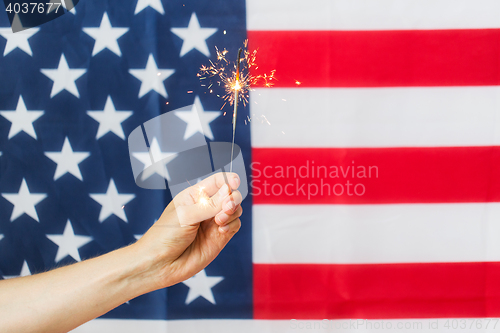 Image of close up of hand with sparkler over american flag