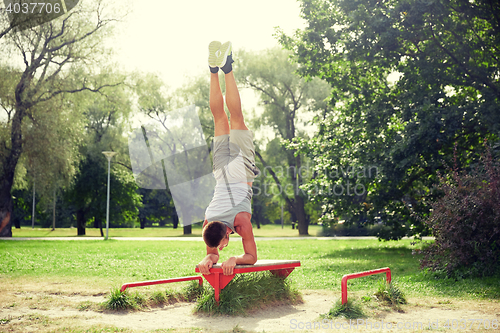 Image of young man exercising on bench at summer park