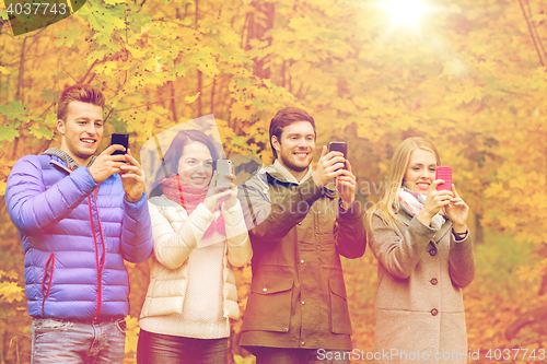 Image of smiling friends with smartphones in city park