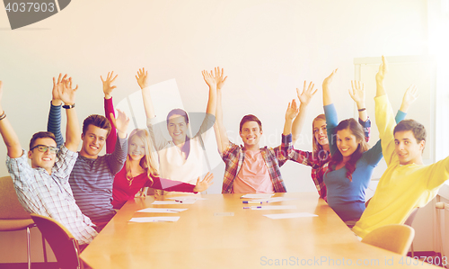 Image of group of smiling students raising hands in office