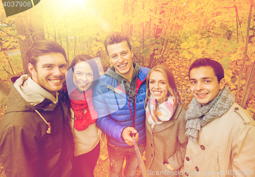 Image of smiling friends taking selfie in autumn park