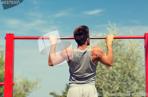 Image of young man exercising on horizontal bar outdoors