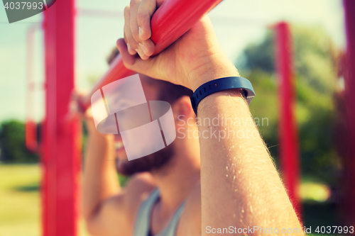 Image of young man exercising on horizontal bar outdoors