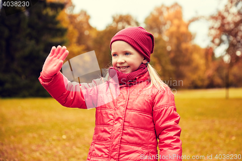 Image of happy little girl waving hand in autumn park