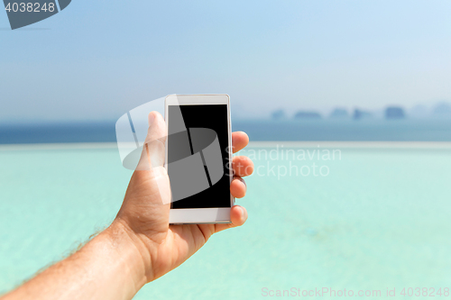Image of close up of male hand holding smartphone on beach
