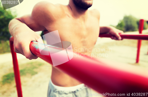 Image of young man exercising on parallel bars outdoors