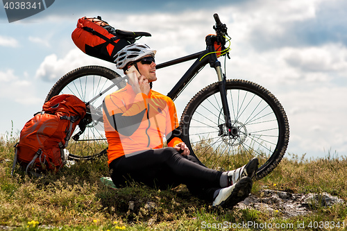 Image of Young man sitting near the cycle on a green meadow