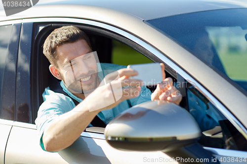 Image of happy smiling man with smartphone driving in car