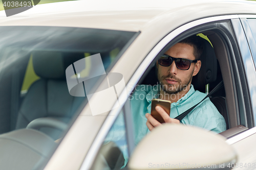 Image of man in sunglasses driving car with smartphone