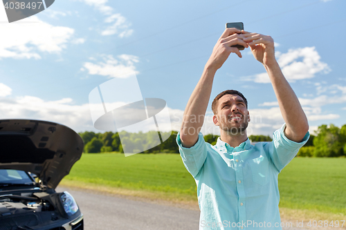 Image of man with smartphone and broken car at countryside