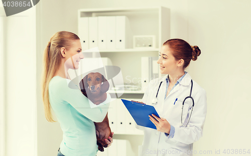 Image of happy woman with dog and doctor at vet clinic