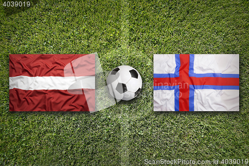 Image of Latvia and Faroe islands flags on soccer field