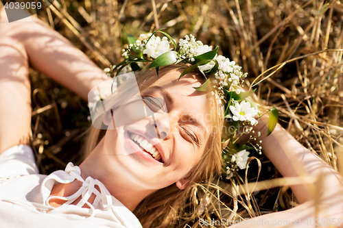 Image of happy woman in wreath of flowers lying on straw