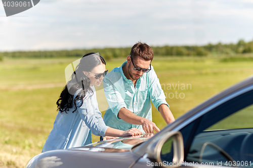 Image of happy man and woman with road map on car hood