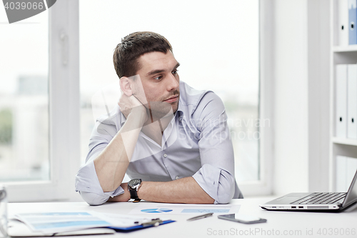 Image of bored businessman with laptop and papers at office