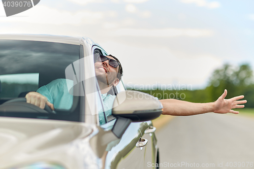 Image of happy man in shades driving car and waving hand