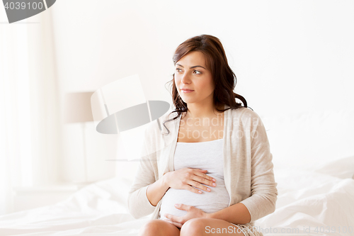 Image of happy pregnant woman sitting on bed at home