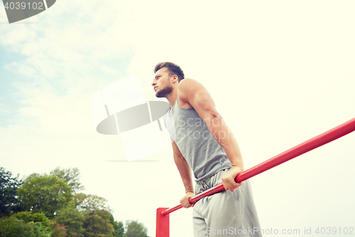 Image of young man exercising on horizontal bar outdoors