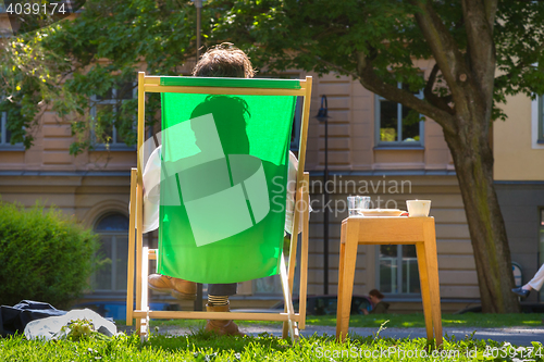 Image of Silhouette of relaxed man on deckchair in a park