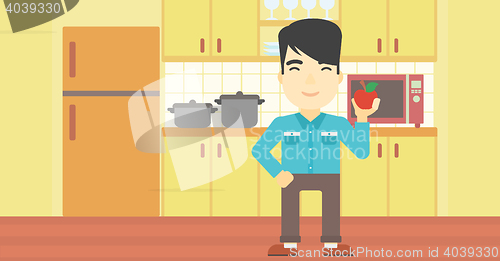 Image of Young man with apple in the kitchen.