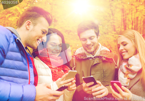 Image of smiling friends with smartphones in city park